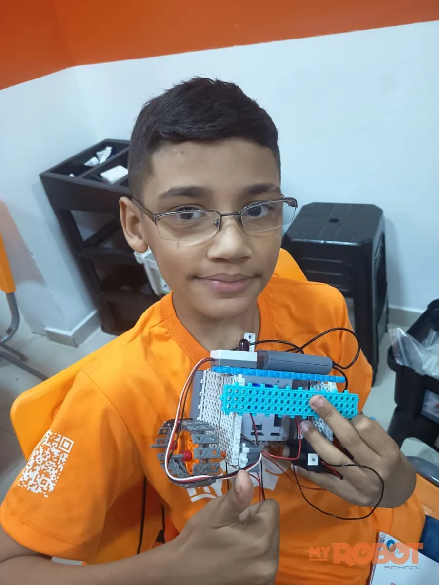Menino de óculos mostrando o carrinho que montou na aula de Firstbot